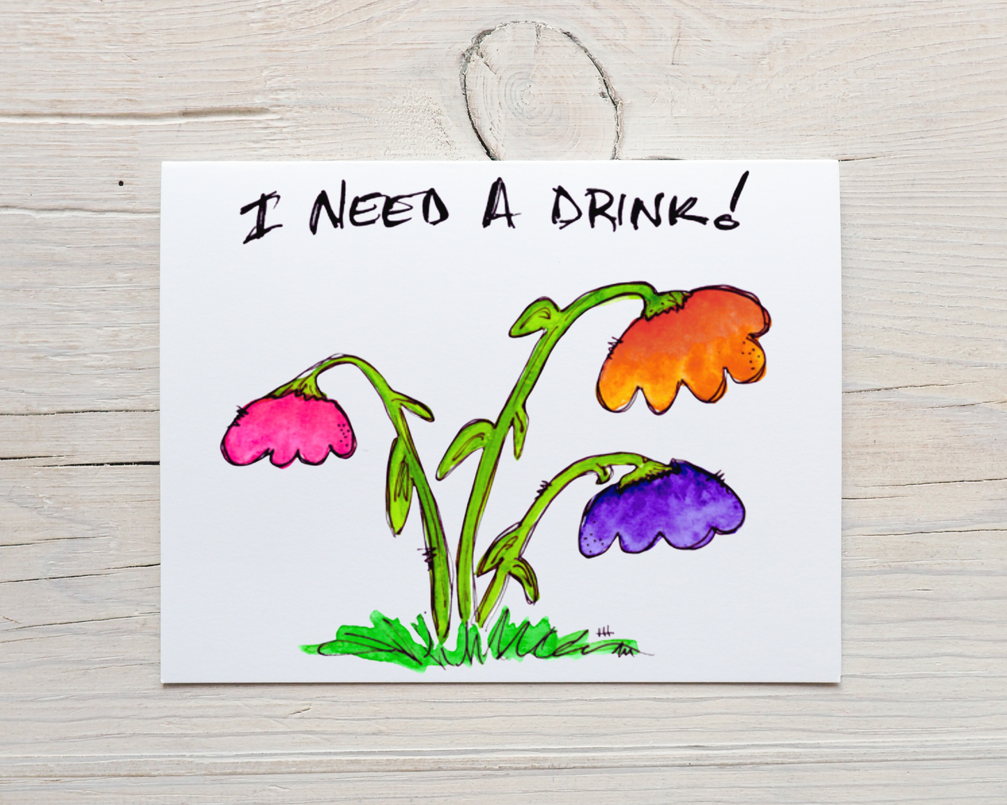 d it on a background of white-washed wood Front of card-- front side of hand-drawn, hand-painted card of a colorful, whimsical watercolor drooping flowers, with the words "I Need A Drink!" across the top, on a background of white-washed wood 