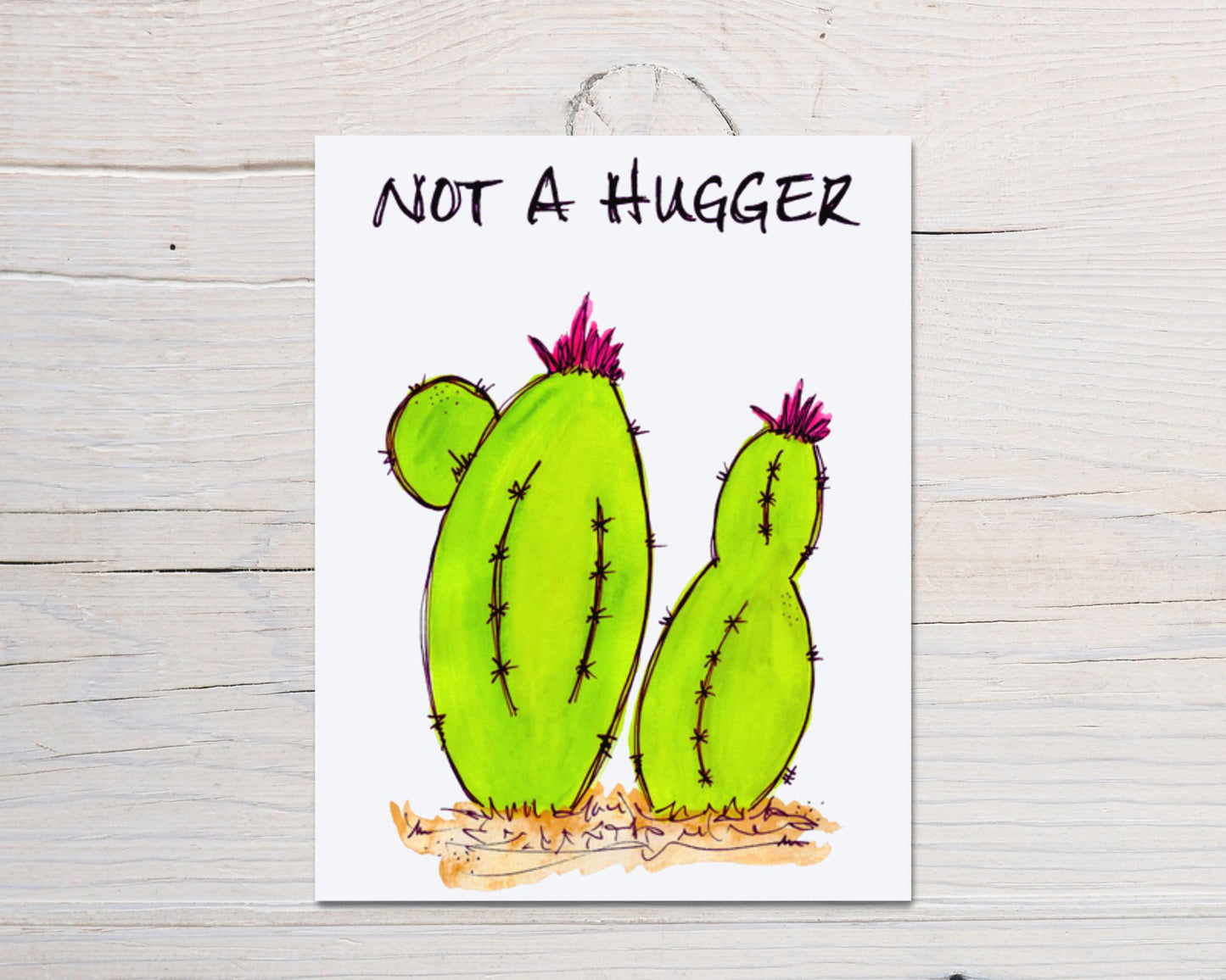front side of hand-drawn, hand-painted card of a colorful, whimsical watercolor lime green cacti with the words "Not A Hugger" across the top, on a background of white-washed wood 