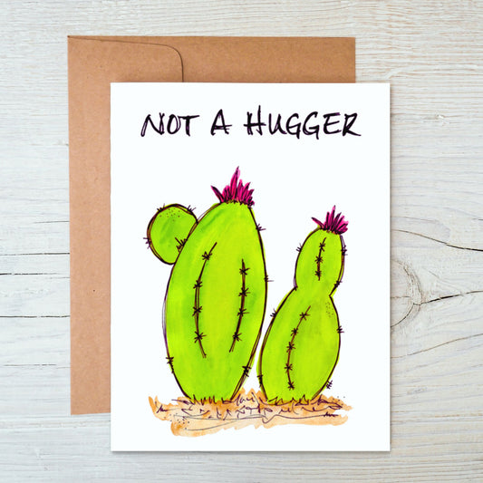 front side hand-drawn, hand-painted card of a colorful, whimsical watercolor lime green cacti with the words "Not A Hugger" across the top, with brown kraft envelope behind it on a background of white-washed wood